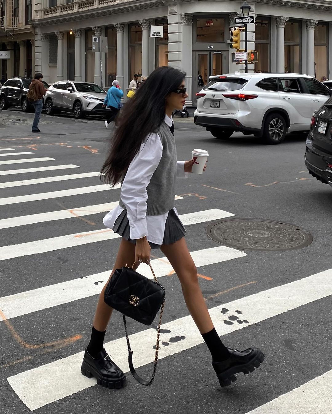 Fashionable woman in white shirt, skirt, chunky boots, and Chanel bag crossing city street