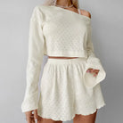 White two-piece outfit consisting of a cropped long-sleeve top and matching shorts with a delicate eyelet pattern.