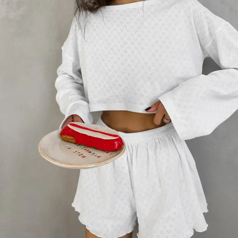 Red eclair-shaped pastry on a white plate held by a person wearing a white crop top and shorts.