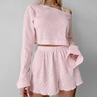 Pink two-piece outfit consisting of a cropped long-sleeve top and matching shorts with a textured pattern.