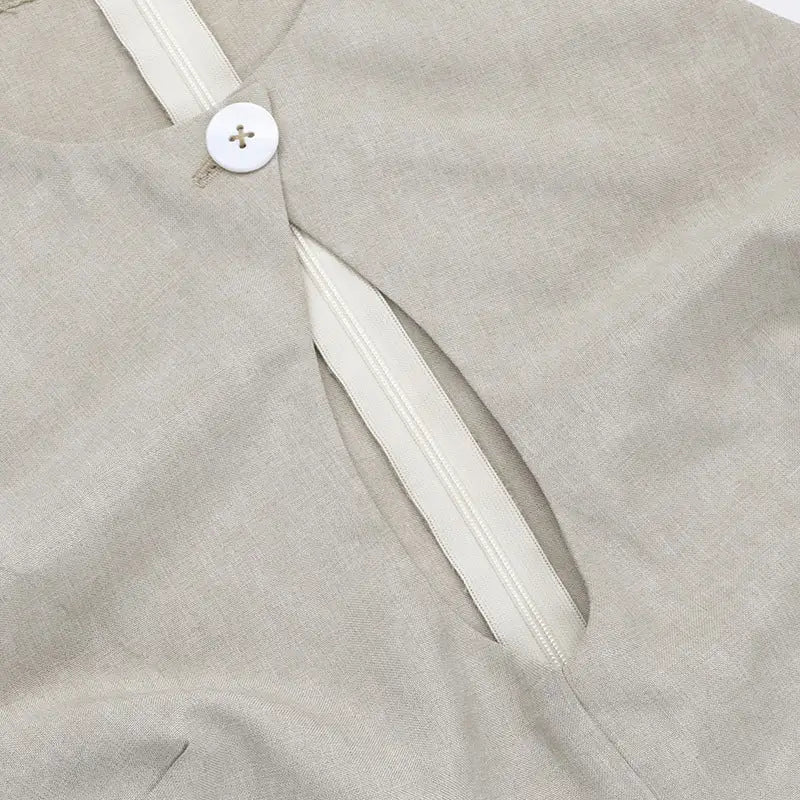 Close-up of a light-colored fabric garment with a white button and zipper detail.