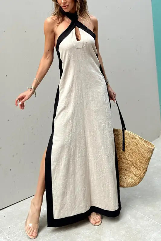 Long white halter-neck maxi dress with black trim and side slits.