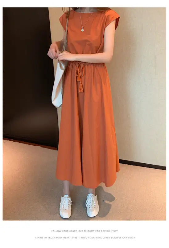 Orange maxi dress with cap sleeves and a drawstring waist, paired with white sneakers and a shoulder bag.