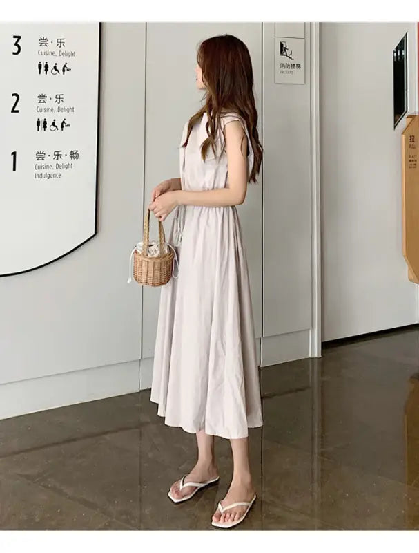 Woman wearing a long white sleeveless dress and carrying a small wicker basket.