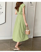 Light green midi dress with cap sleeves and a cinched waist, paired with a small wicker handbag.