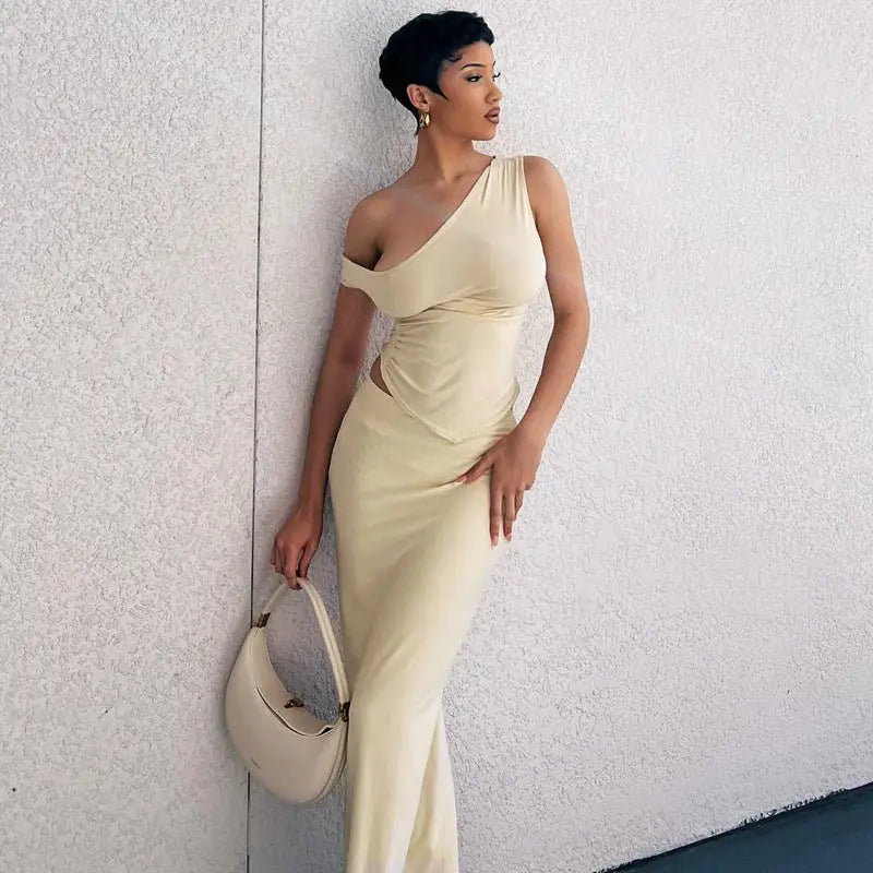 Woman wearing an elegant one-shoulder cream-colored gown and holding a matching handbag.