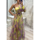 One-shoulder floral maxi dress with yellow and purple tones, featuring a high slit and sheer fabric.