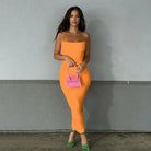 Woman wearing a vibrant orange bodycon dress and holding a small pink handbag.