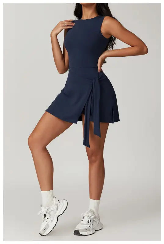 Navy blue sleeveless mini dress with a pleated skirt detail worn with white socks and chunky sneakers.