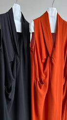 Two sleeveless dresses on hangers, one black and one orange.