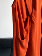 Bright orange flowing fabric garment with draped folds and a pocket.