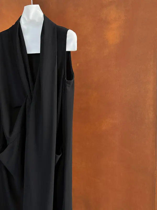 Black sleeveless wrap dress or top hanging on a white hanger.