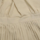 Beige pleated fabric with a waistband, likely part of a dress or skirt.