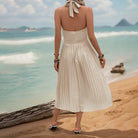 Woman wearing a white halter-neck pleated sundress on a beach.