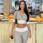 Woman with long dark hair wearing a gray and white crop top and matching pants, standing in front of a bakery counter.