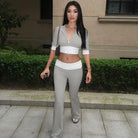 Young woman in a white crop top and gray flared pants posing outdoors.