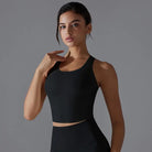 Young woman wearing a black crop top and posing with one hand near her neck.