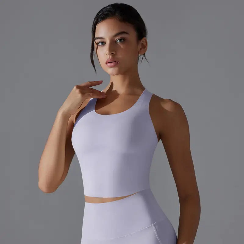 Young woman wearing a white athletic crop top and posing with one hand near her neck.