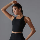 Young woman wearing a black crop top and posing with one arm raised.