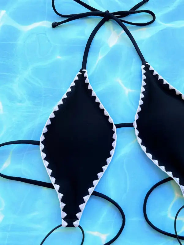 Black bikini top with white zigzag trim against a blue watery background.