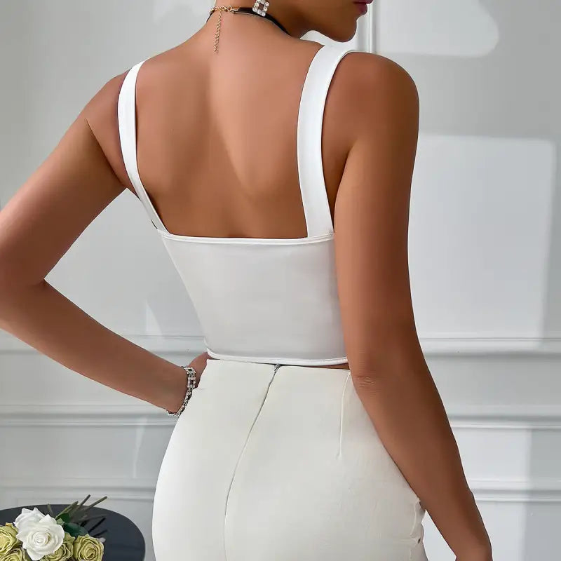 White sleeveless top with wide straps and a square back, paired with a high-waisted white skirt or pants.