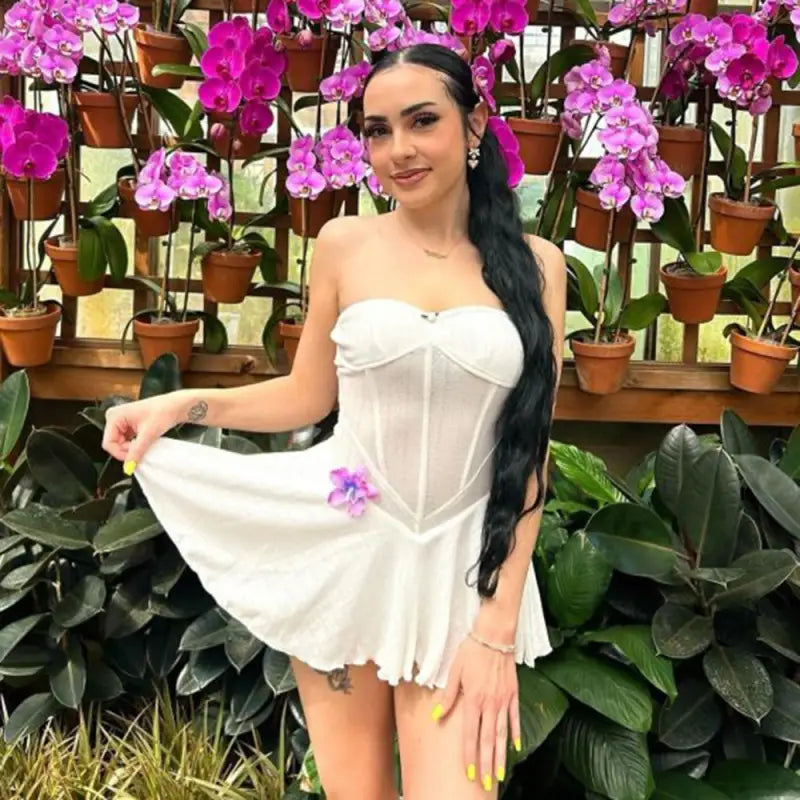 Woman in a white strapless mini dress posing among orchid plants.