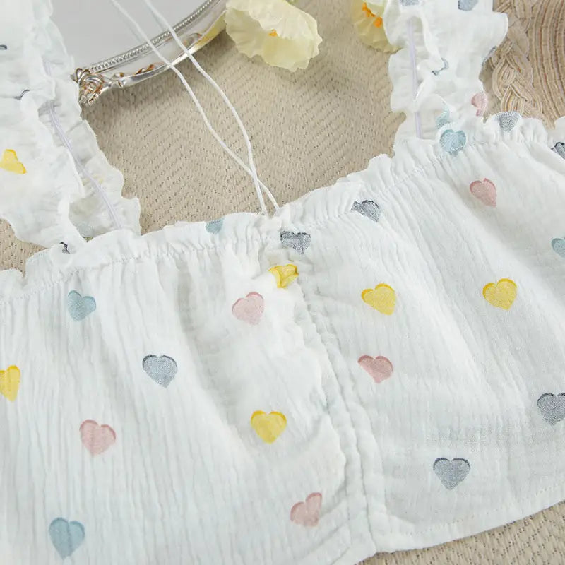 White crop top with pastel-colored heart patterns and thin shoulder straps.