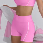 Bright pink workout set consisting of a crop top and high-waisted shorts with white piping.