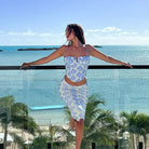 Woman in a blue and white floral two-piece outfit posing on a balcony overlooking the ocean.