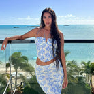 Woman in a blue and white floral two-piece outfit posing on a balcony overlooking a tropical beach.