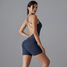 Woman wearing a navy blue workout bodysuit with crisscross back straps.